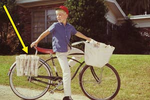 A boy with a cap delivers newspapers on a bike in front of a house