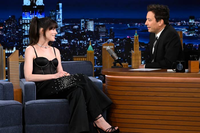 Anne Hathaway in a black dress with Jimmy Fallon on a talk show set