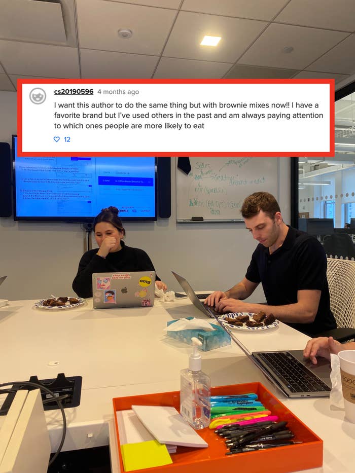 Two people at a table with laptops, sampling brownies during a meeting. Whiteboard with writing in the background