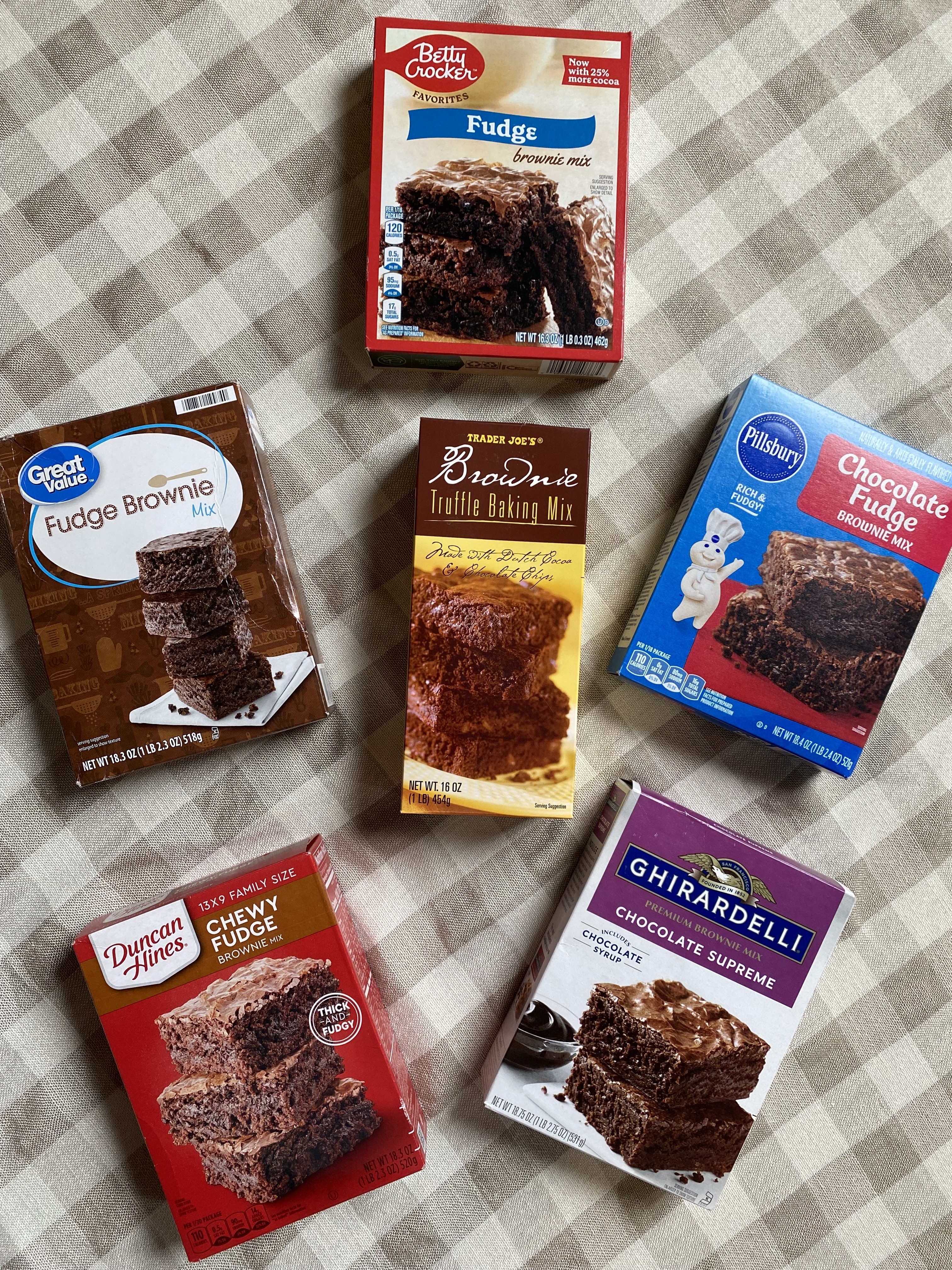 Six boxed brownie mix brands arranged on a patterned fabric