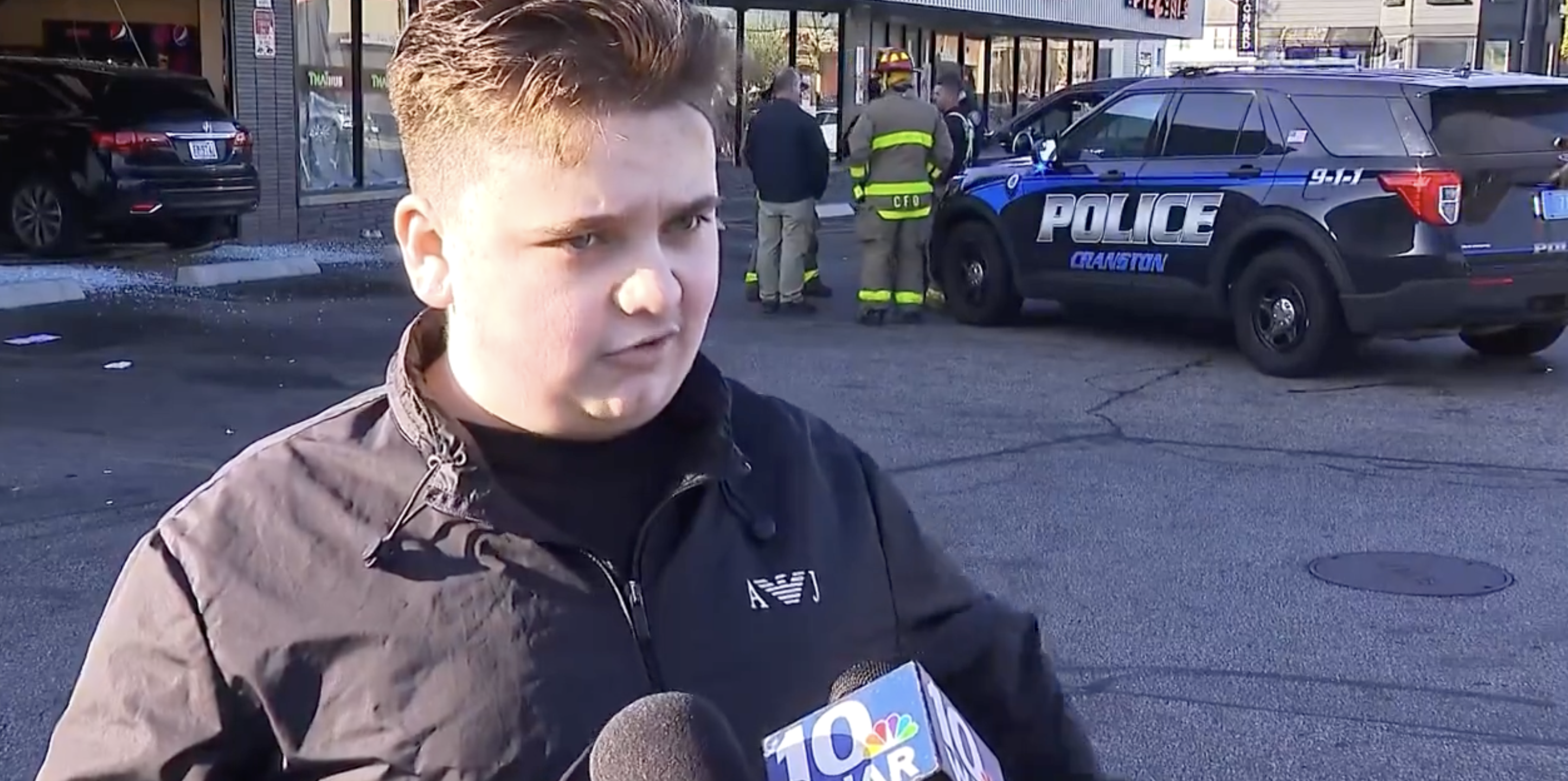 Person being interviewed by news crew with police and emergency vehicles in the background