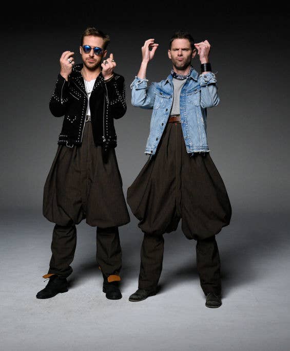 Two men successful  unsocial   oversized pants and jackets posing with hands raised