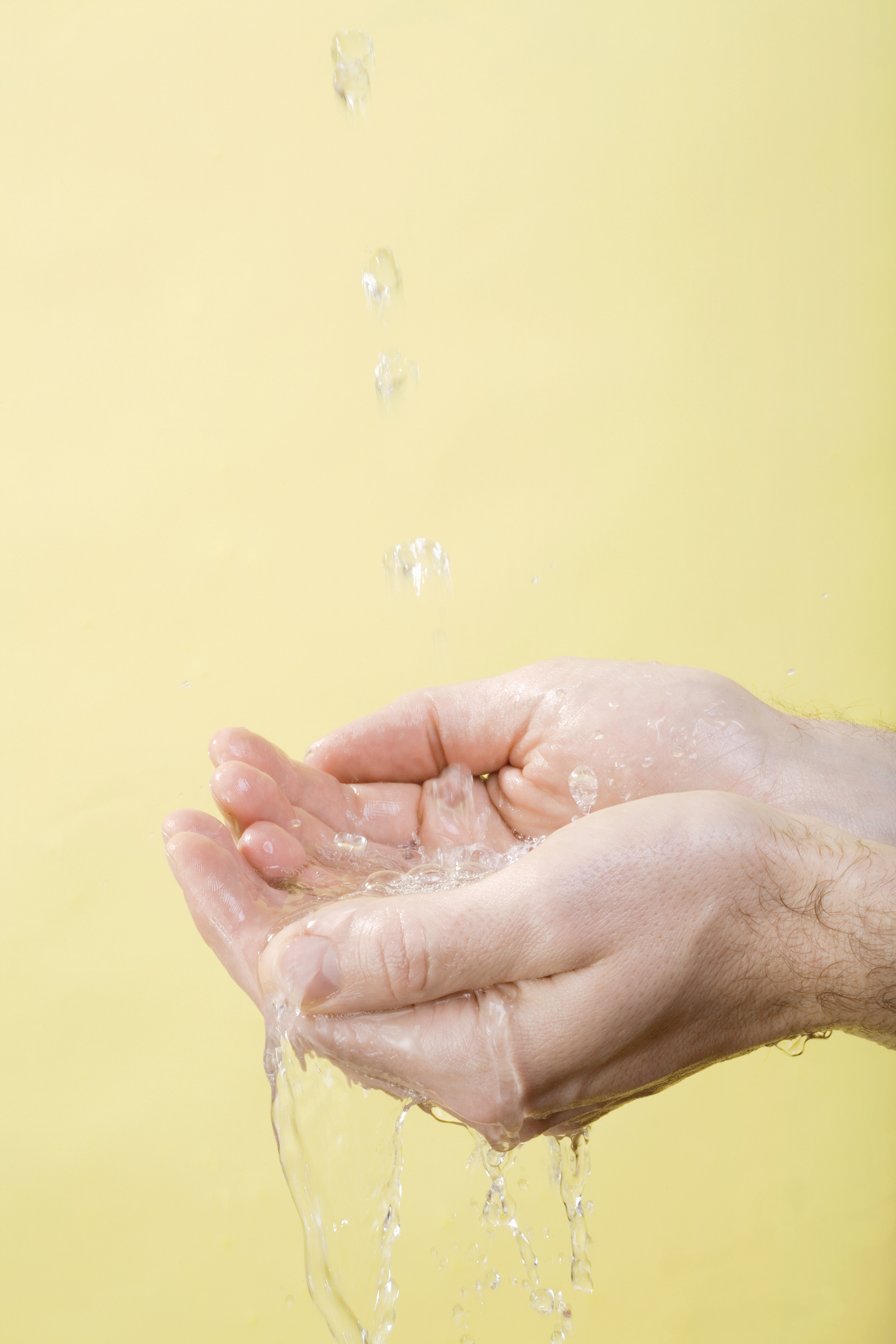 Person catching dripping water in their hands against a yellow background