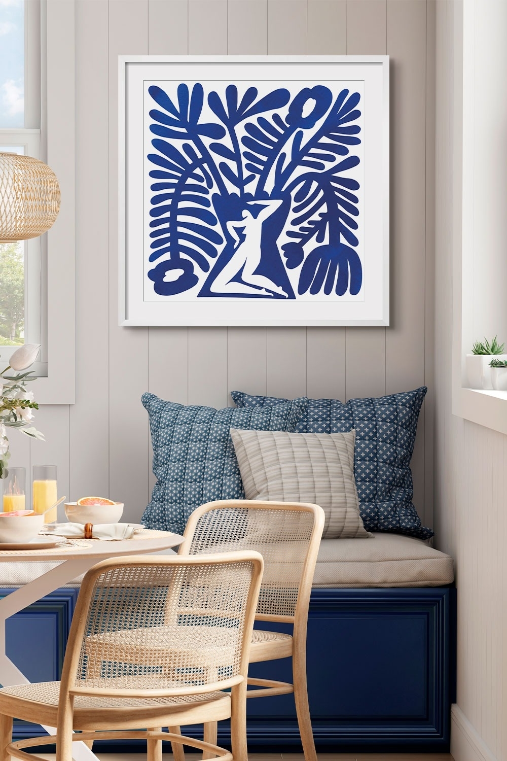 Artwork featuring a botanical silhouette hangs above a bench with cushions in a breakfast nook