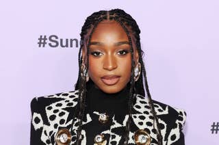 Woman in patterned jacket poses for photo, wearing braided hair and statement earrings