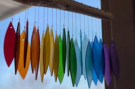 Hanging glass suncatchers in various shapes and primary colors against a clear window with visible sky