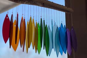 Hanging glass suncatchers in various shapes and primary colors against a clear window with visible sky