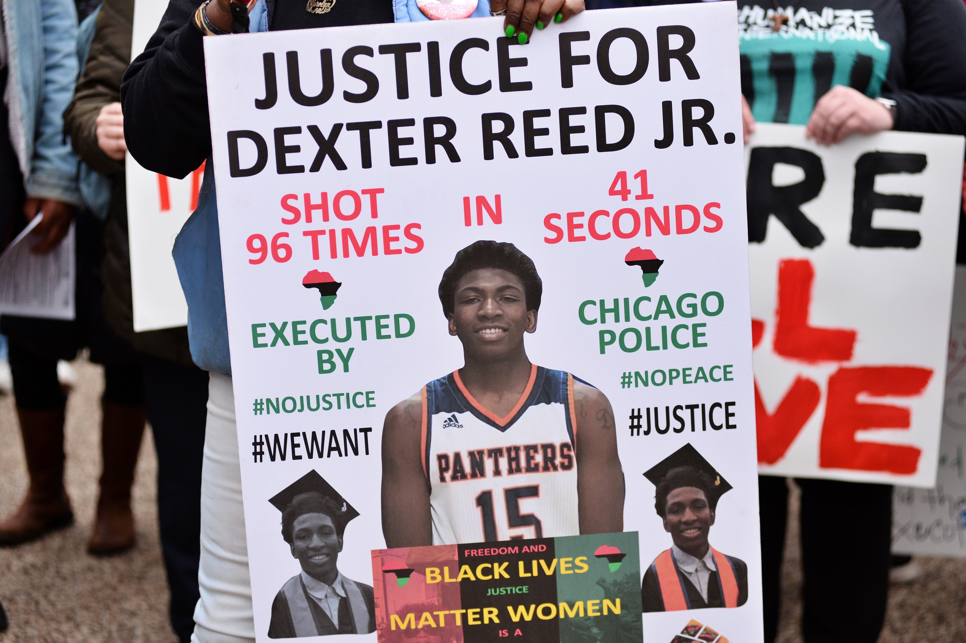 Person holding a sign with text &quot;Justice for Dexter Reed Jr.&quot; with details of his shooting and support for Black Lives Matter