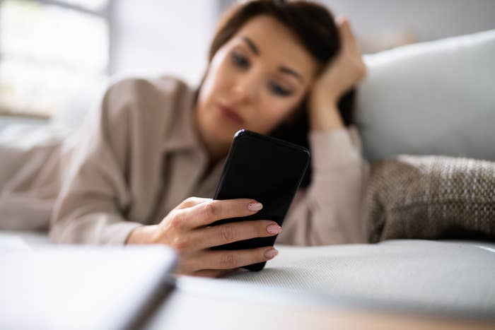 Woman lying on a couch looking at her smartphone with focus on her hand and phone