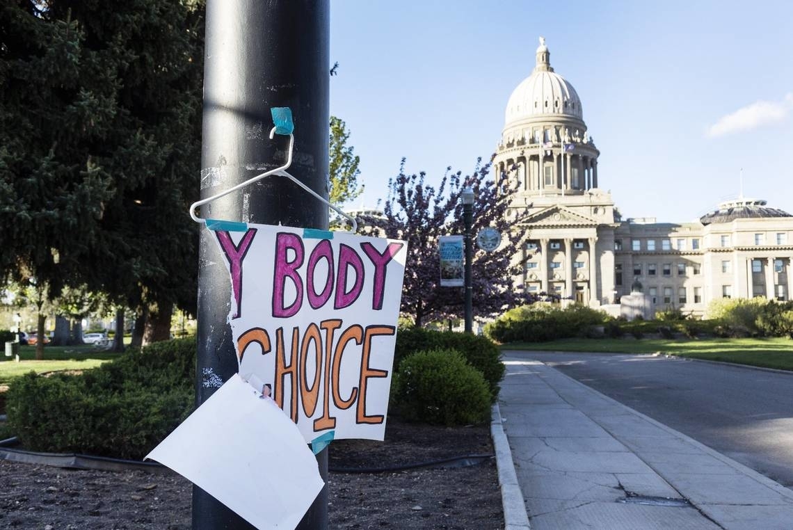 Handmade sign reading &quot;MY BODY MY CHOICE&quot; on a post, with a blurred capitol building in the background