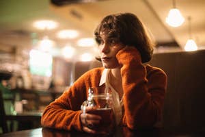 Woman in a cozy sweater sitting in a cafe, holding a mug, appearing contemplative