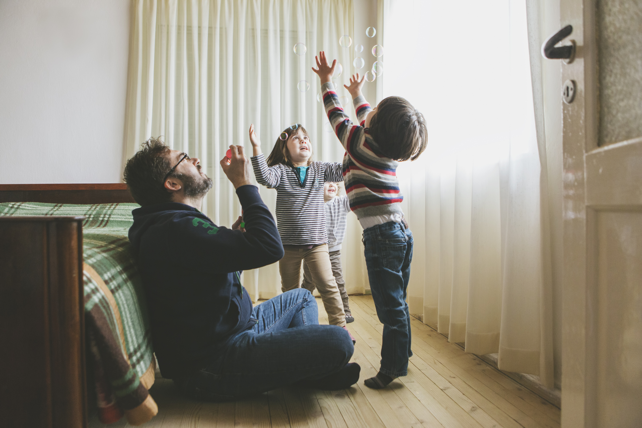 Man and two kids playfully toss coins in a cozy room, depicting a family enjoying a simple, budget-friendly activity