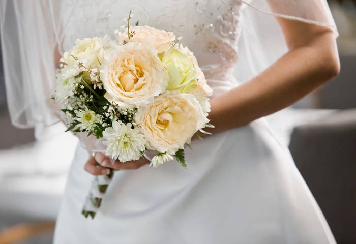 Bride holding a bouquet of roses and assorted flowers, details of lace dress visible