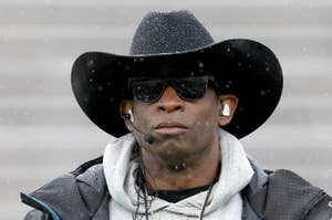 Person in cowboy hat and sunglasses, with earphones, and a rucksack. Raindrops are visible around them