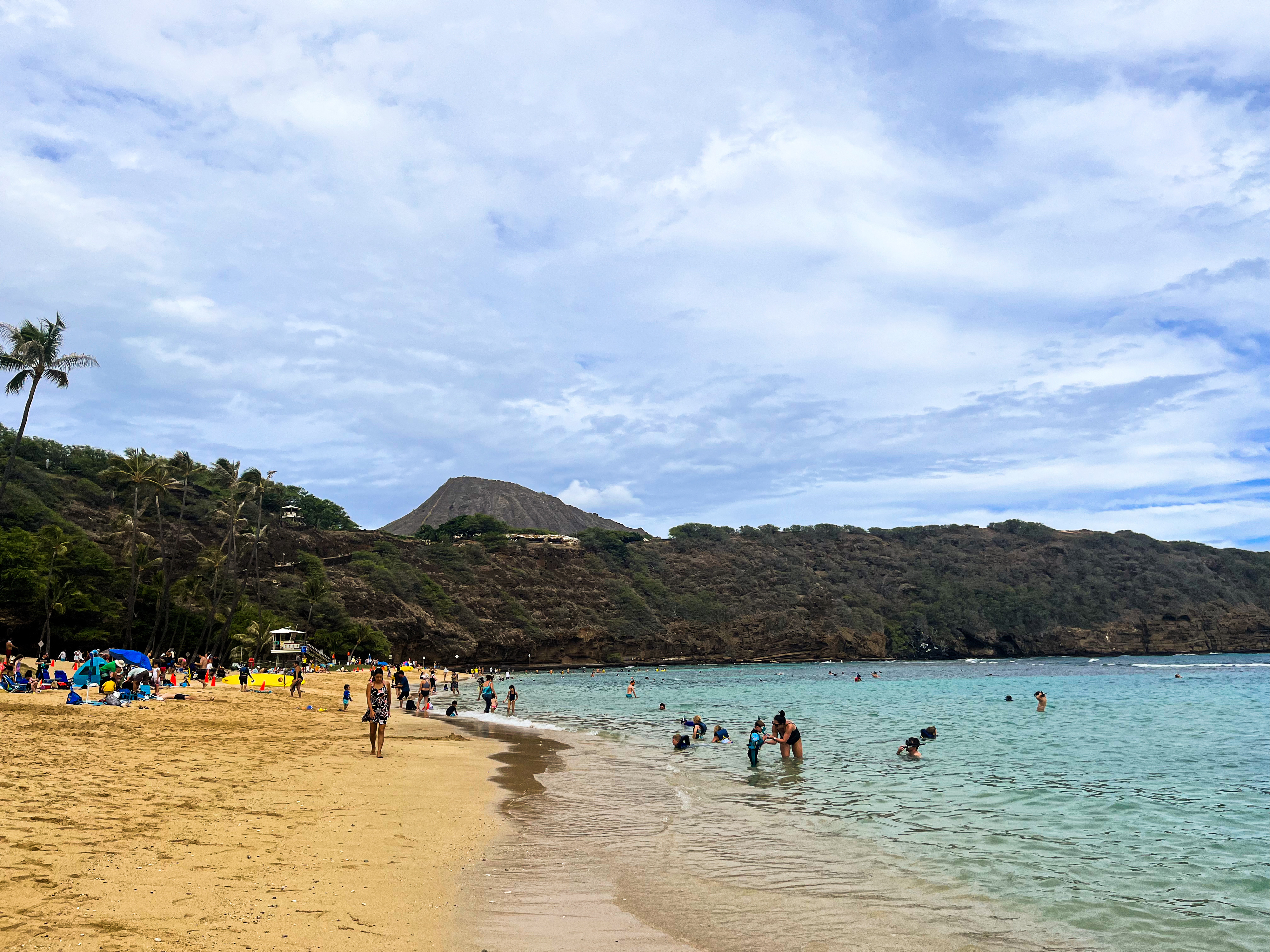 Beachgoers at a sandy beach with a mountain in the background and scattered clouds above