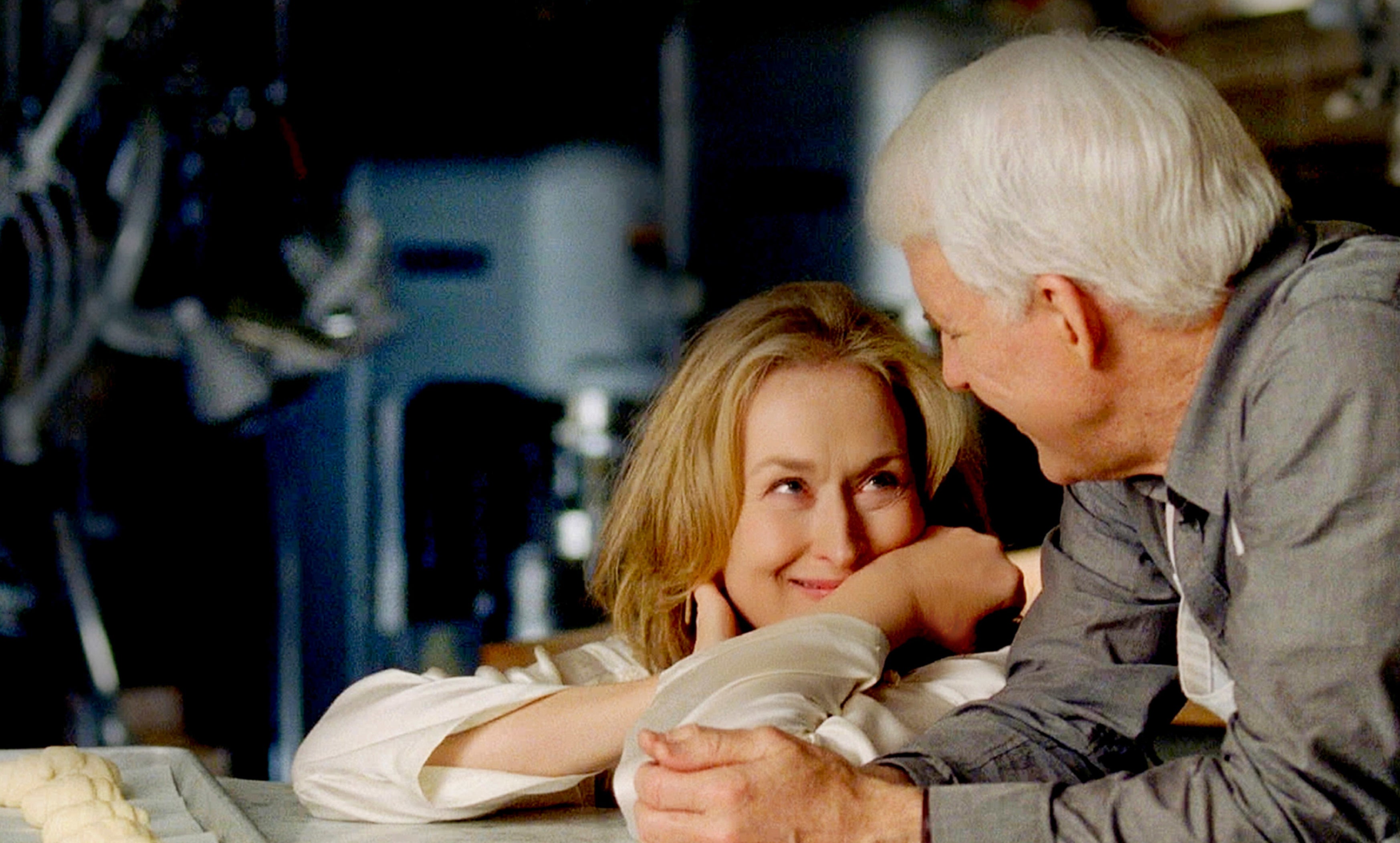 Meryl Streep and Steve Martin in a scene, leaning on a kitchen counter, sharing a moment