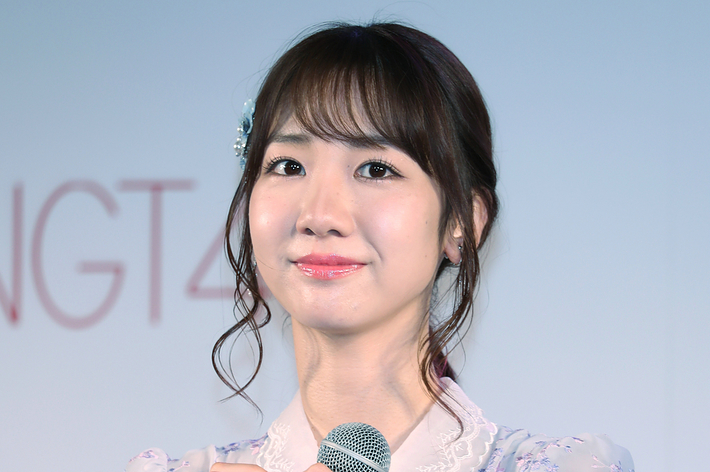 イベントでマイクを持つ女性、ドレスにレースのディテールがある。