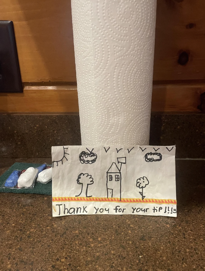 Hand-drawn thank you note with a house and two cars, beside a paper towel roll on a counter