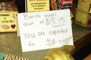 Handwritten sign states "Barista wages start at $5.15. You are expected to tip. Thanks" on a cafe counter