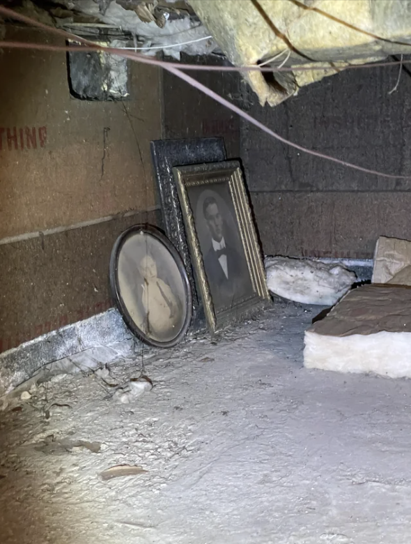 Two framed pictures leaning against a wall in a dim, dusty space