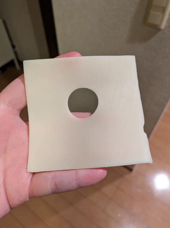 Hand holding a square object with a circular hole in the center