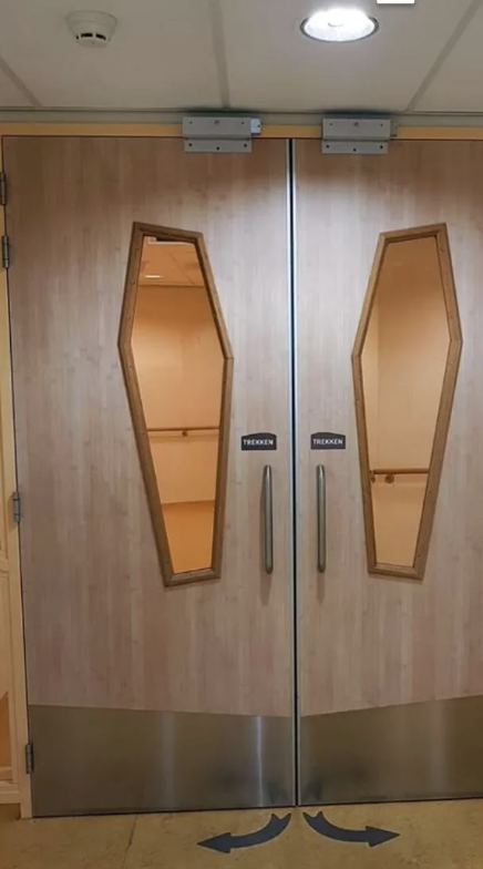 Wooden double doors with vertical handles and coffin-shaped windows. Arrows on floor pointing towards doors