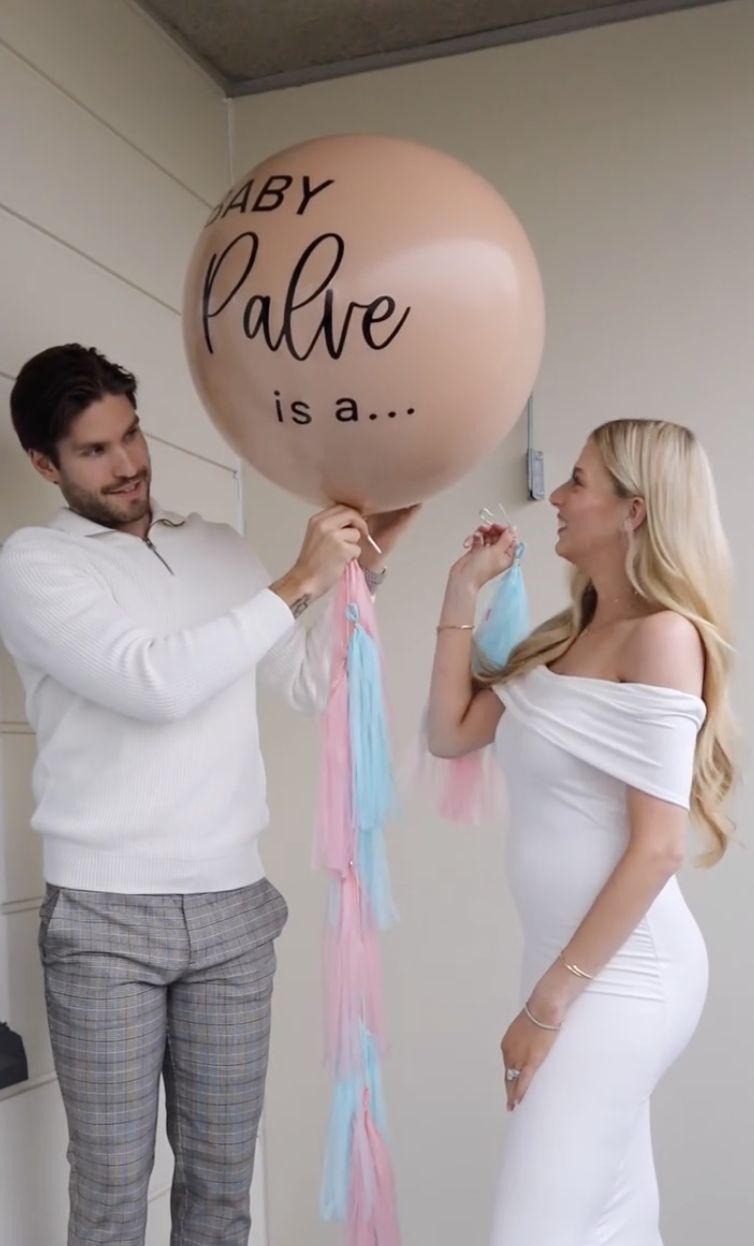 A couple holds a large balloon reading &quot;Baby Palve is a...&quot; for a gender reveal