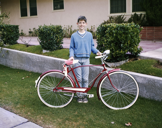 A young boy smiling next to his bicycle