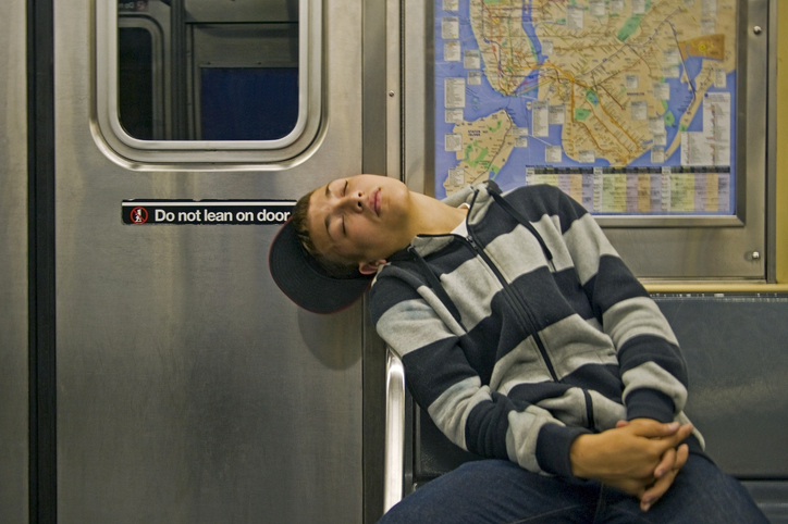 Person sleeping on a subway car seat with head resting against window