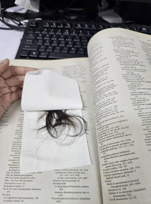 A person&#x27;s hand is holding a napkin with hair on it, placed on an open scientific textbook