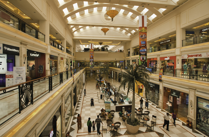 Interior of a multi-level shopping mall with stores, palm trees, and shoppers