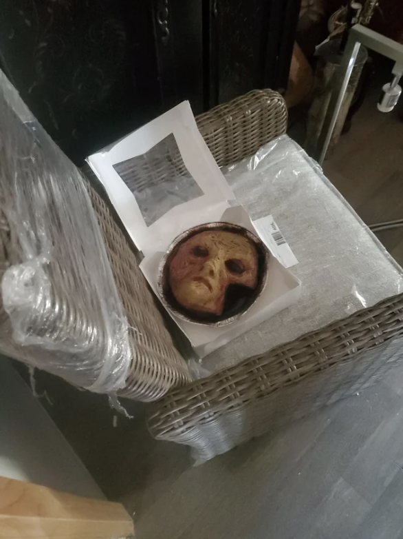 Mask resembling a face placed on top of wrapped furniture, barcode labels visible
