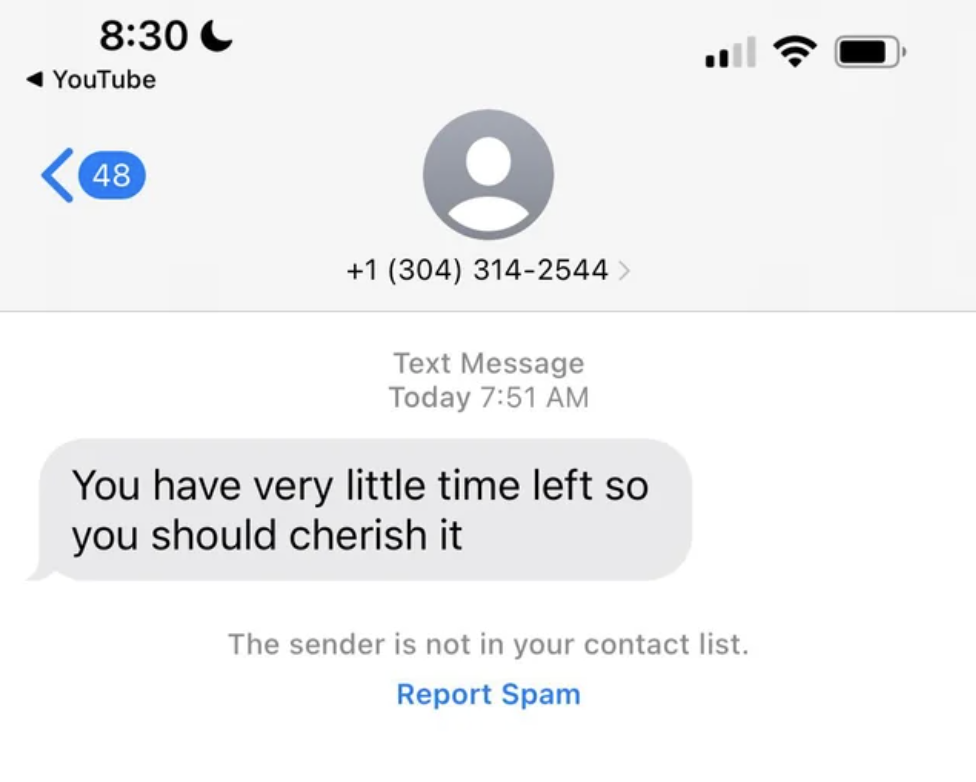 Text message on phone screen with ominous warning to cherish the little time left; option to report as spam is visible
