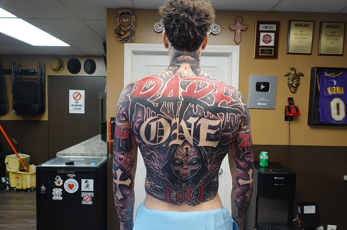 Person displaying extensive back tattoos in a tattoo parlor