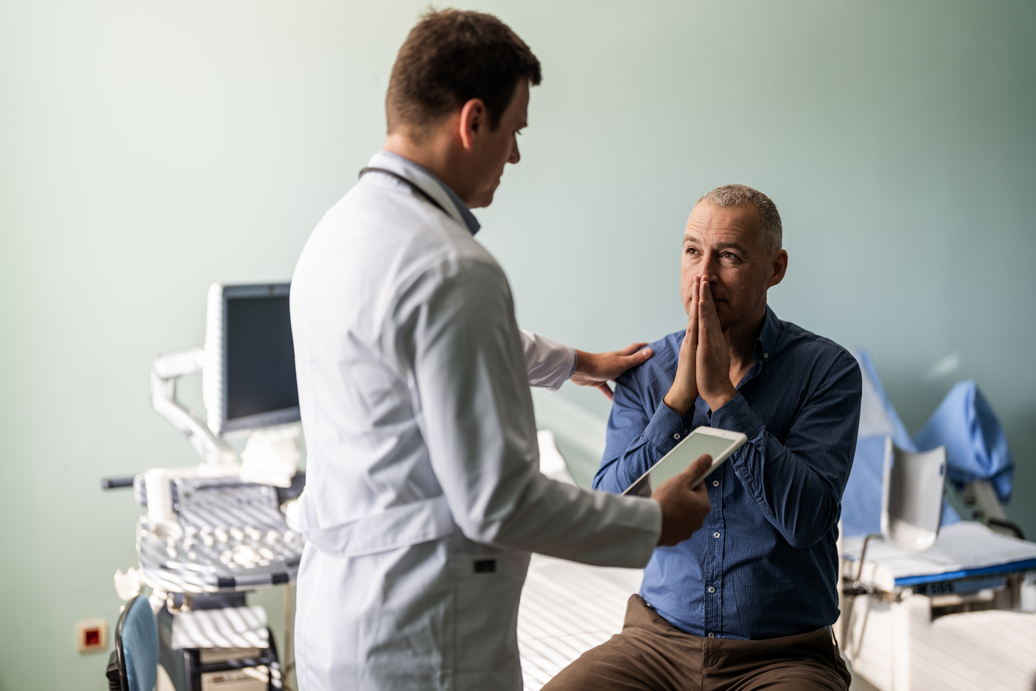 Doctor consulting with patient showing concern, both are gesturing with their hands, in a medical office setting