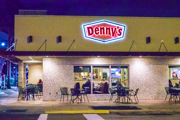 Exterior of a Denny&#x27;s restaurant at night with illuminated signage and visible indoor diners