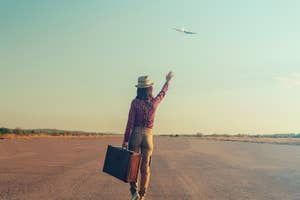 Person with suitcase waving at airplane in sky, indicating travel and departure