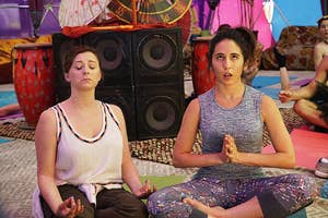 Two women practicing yoga in a room with others, one in a tank top and the other in a sleeveless top