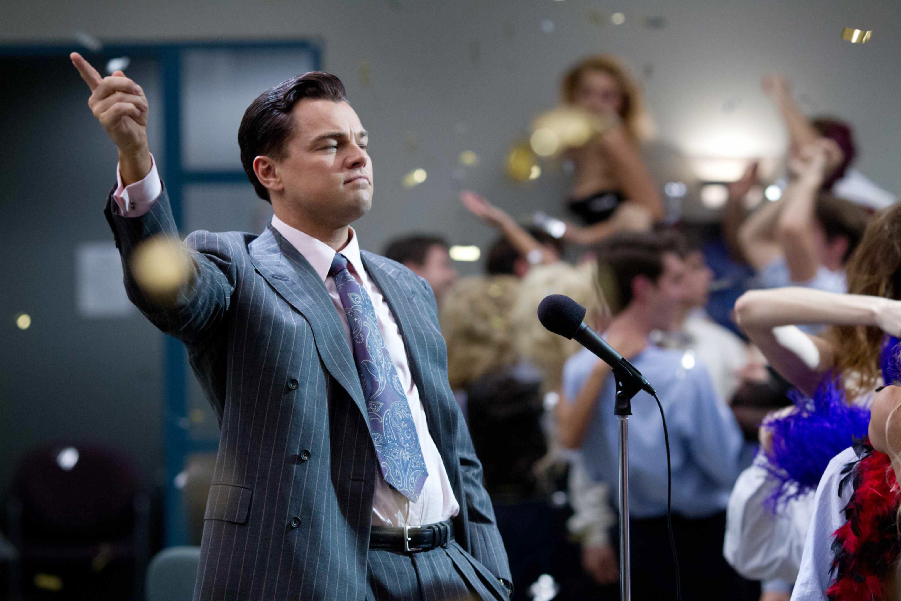 Leonardo DiCaprio as Jordan Belfort in a scene from The Wolf of Wall Street, gesturing triumphantly at a crowded party