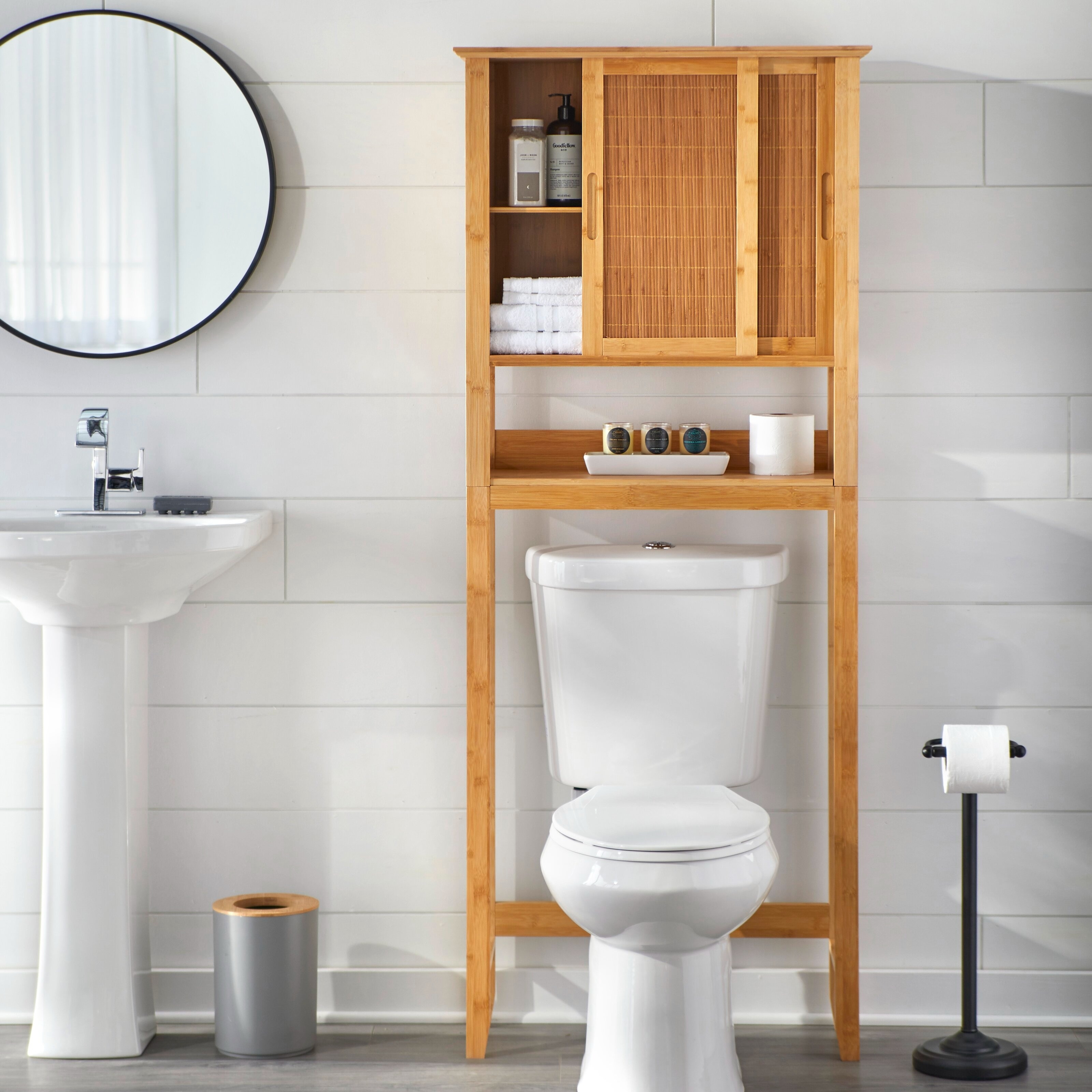 A modern bathroom with a toilet, sink, mirror, and wooden storage cabinet