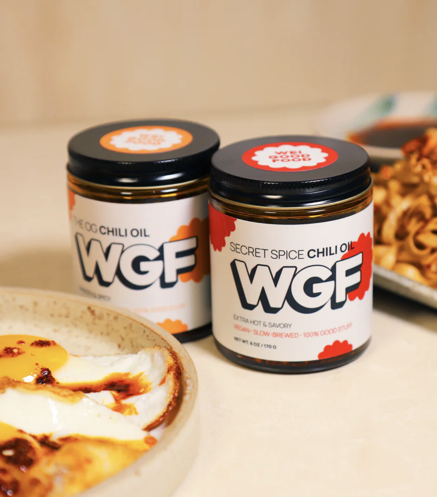 Two jars of WGF Secret Spice Chili Oil next to a bowl of prepared food