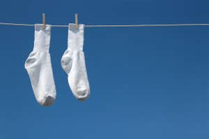 青空の背景に、紐に洗濯バサミで吊るされた白い靴下二つが写っています。