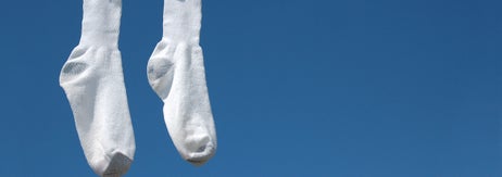 青空の背景に、紐に洗濯バサミで吊るされた白い靴下二つが写っています。