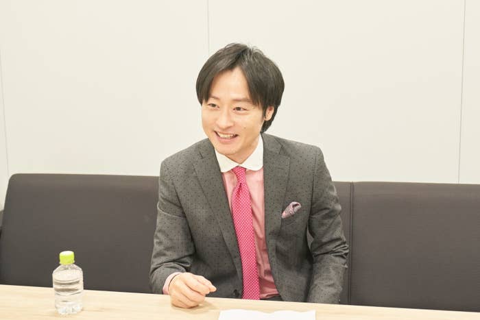 スーツを着た男性がテーブルに座り、笑顔で話している。