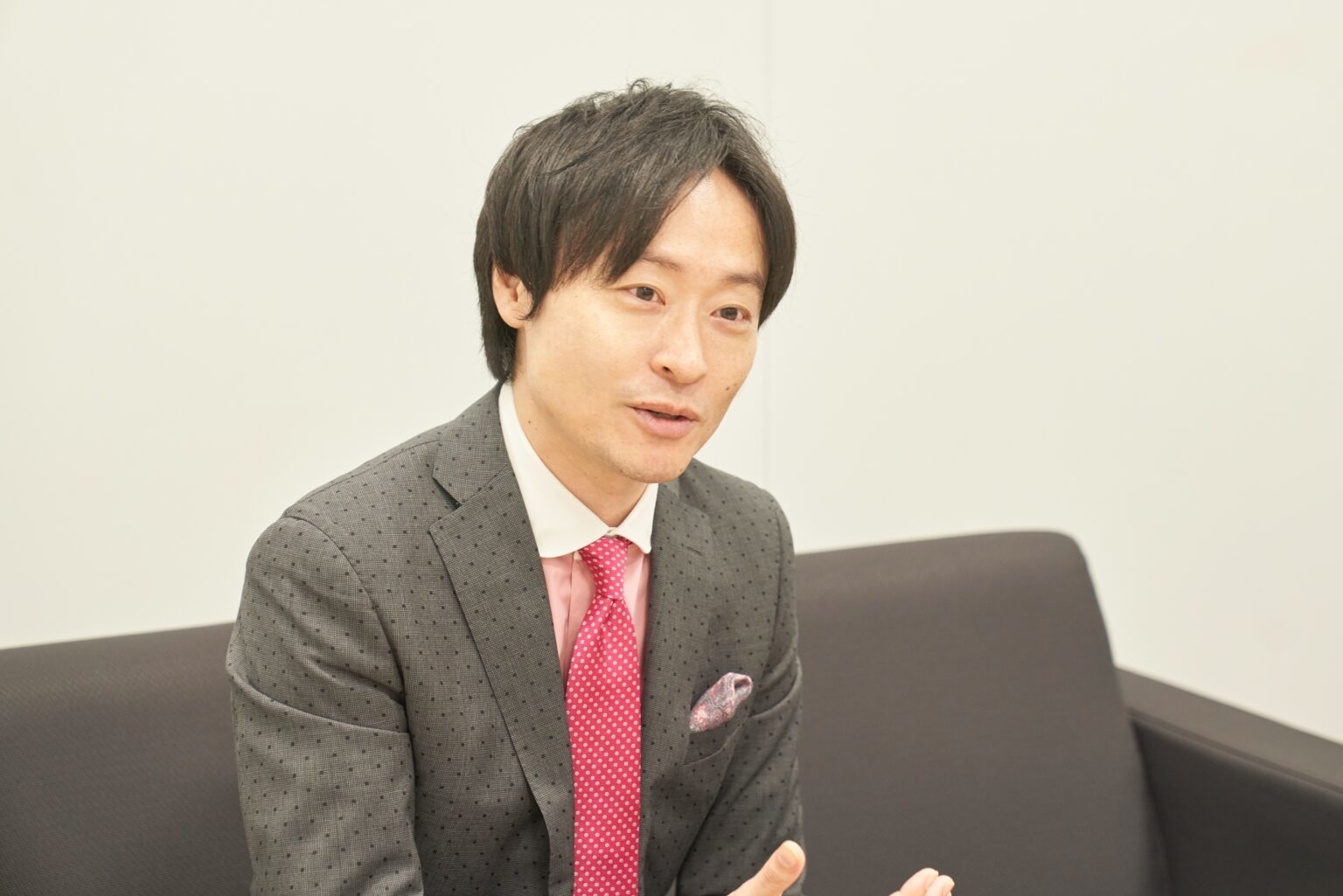 スーツを着た男性がソファに座り、話している様子。