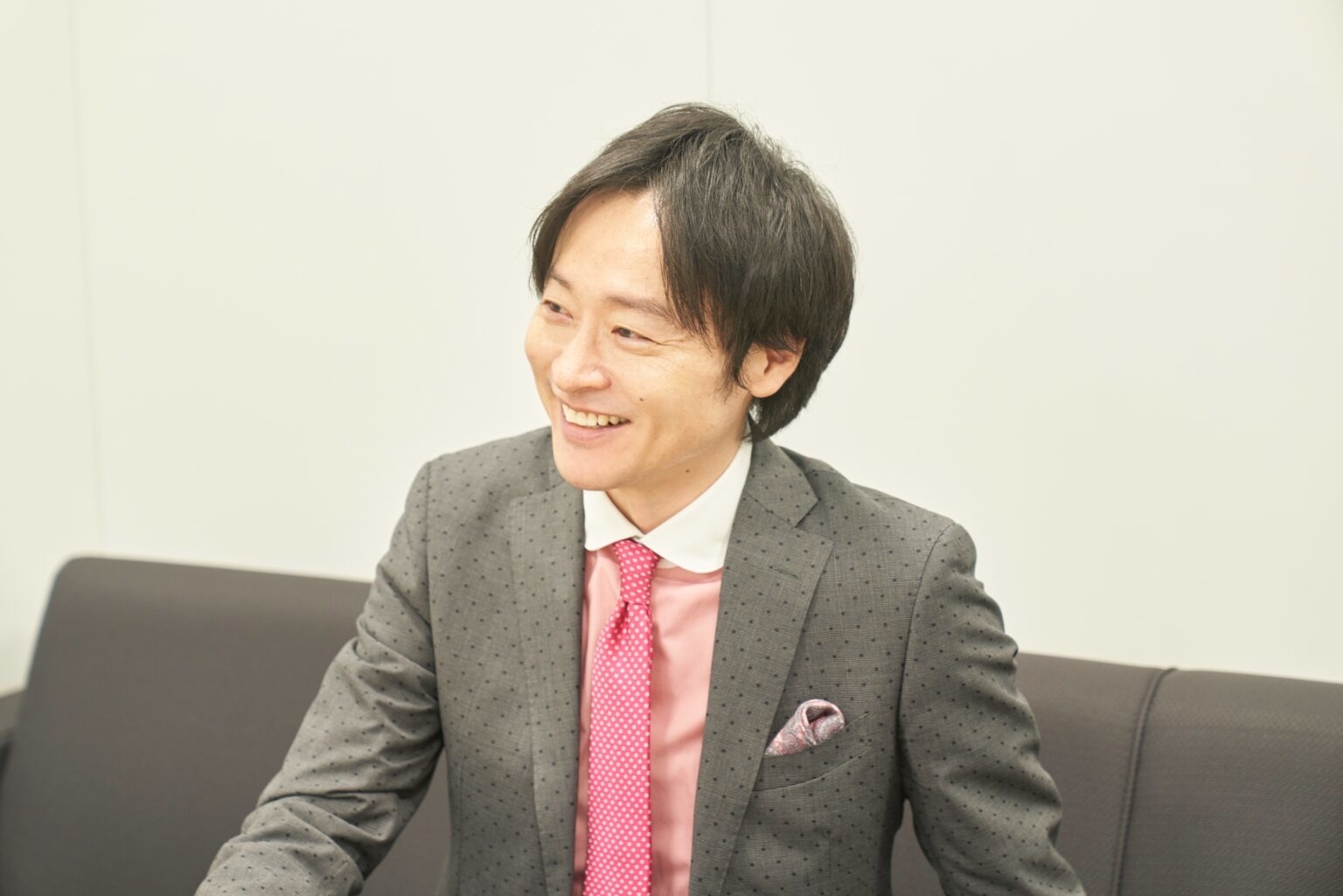 スーツを着た笑顔の人物がソファに座っている。