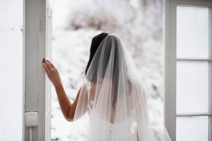 Bride in a white dress and veil looking out of a window with a snowy landscape outside