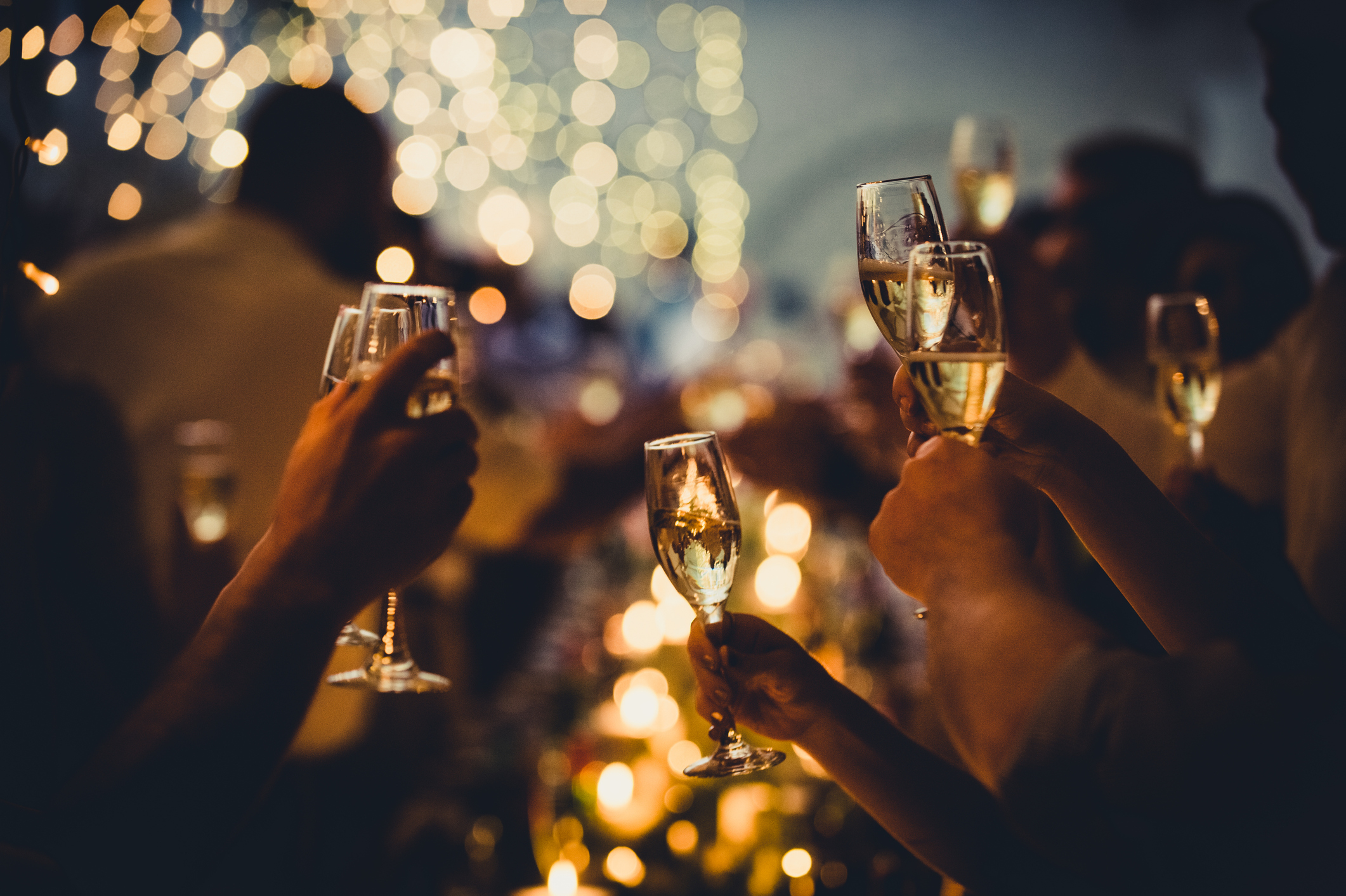 People toasting with champagne glasses at a dimly lit event with bokeh lights in the background