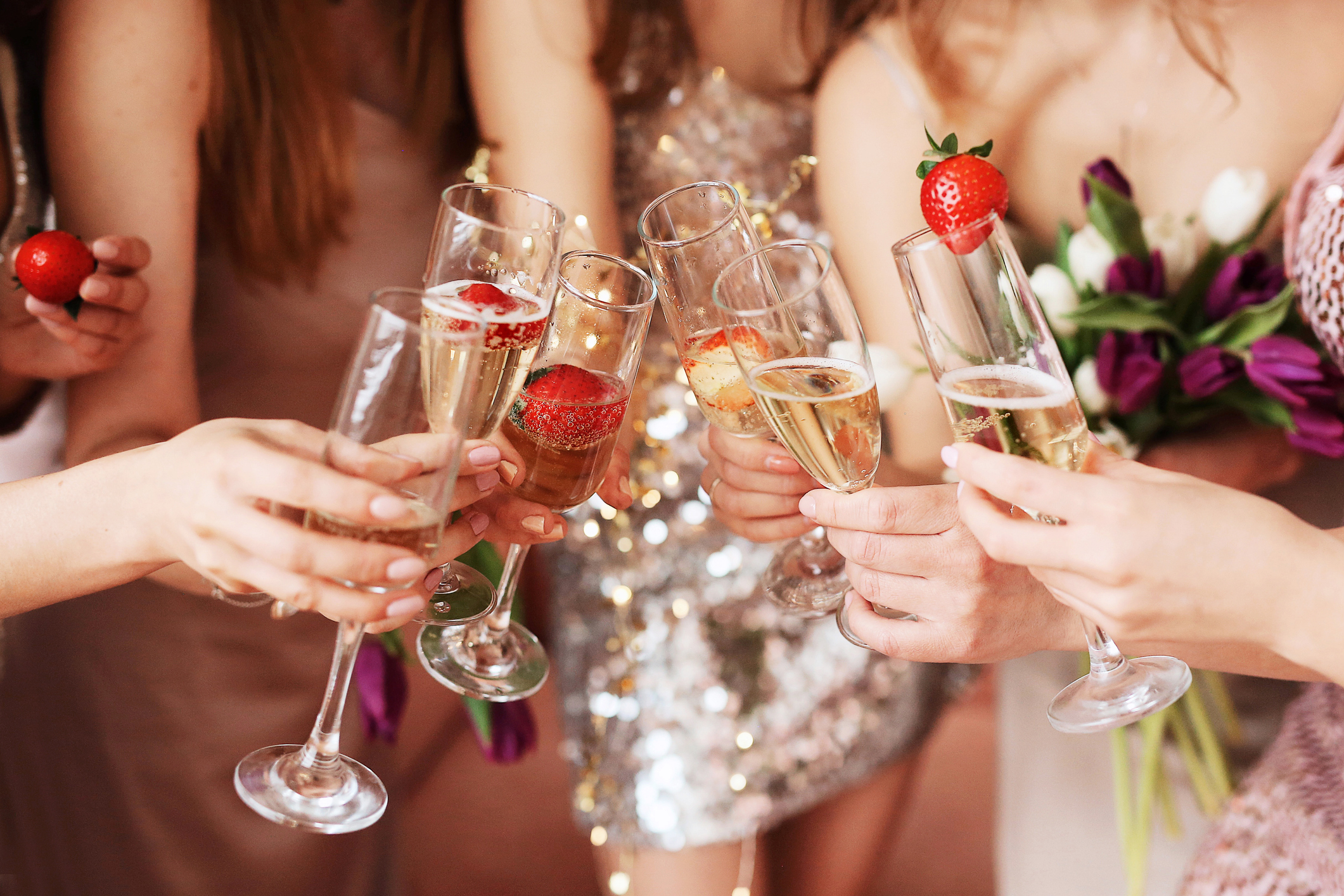 Group of people clinking champagne glasses, one with a strawberry, at a celebration