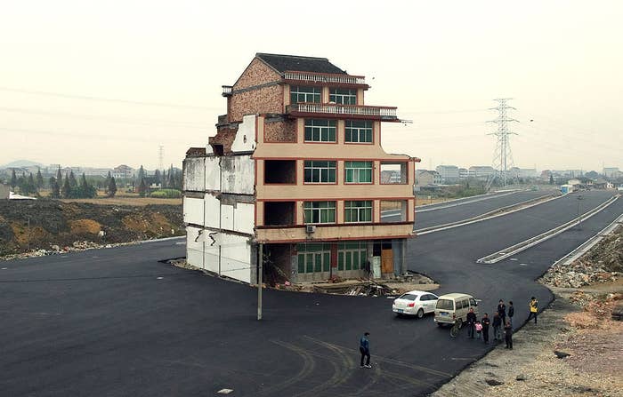Isolated three-story house in the middle of a paved road with a small group of people standing nearby